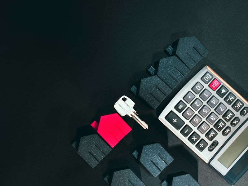 A key, a small house model and a calculator on a dark desk