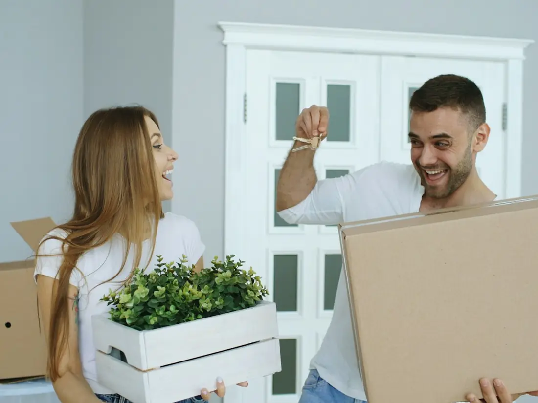 A smiling couple carrying moving boxes into a new home