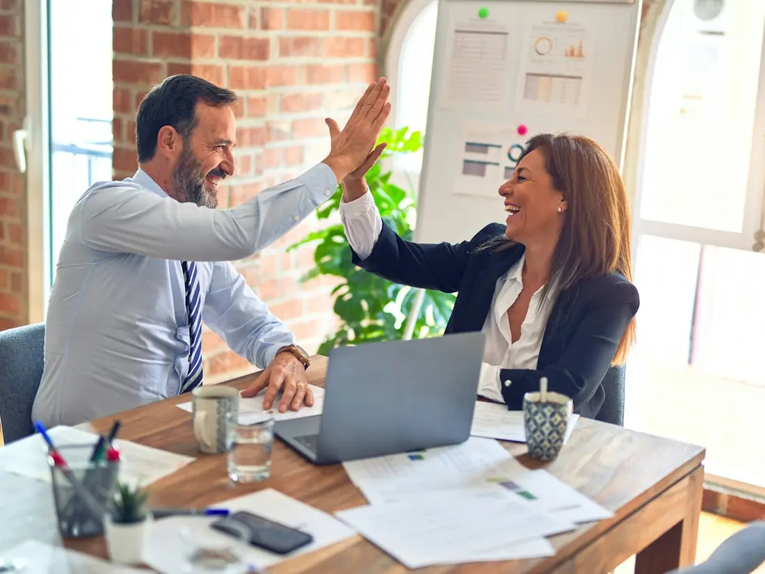 Two colleagues high-fiving across a meeting-room table