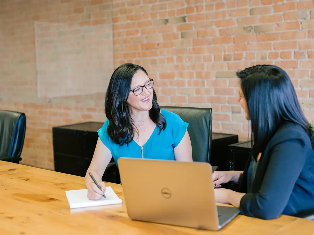 Two women talking at a table with a laptop