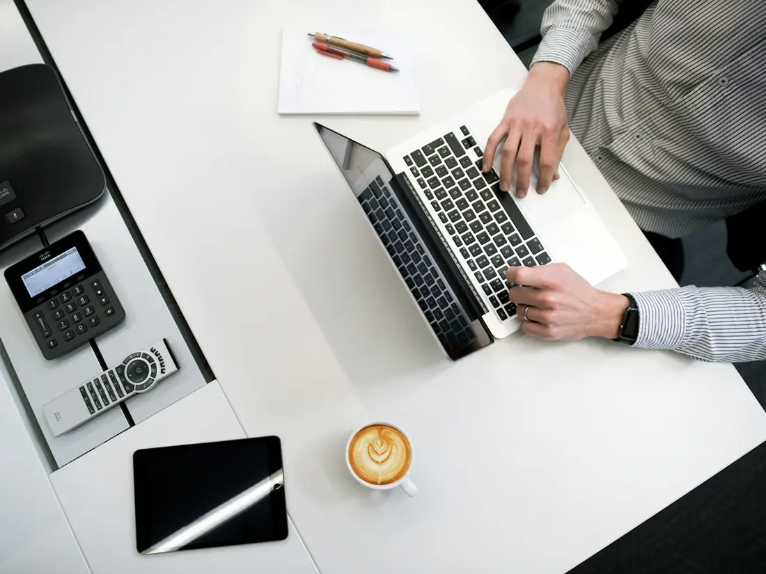 Overhead view of a laptop, tablet and coffee on a white desk