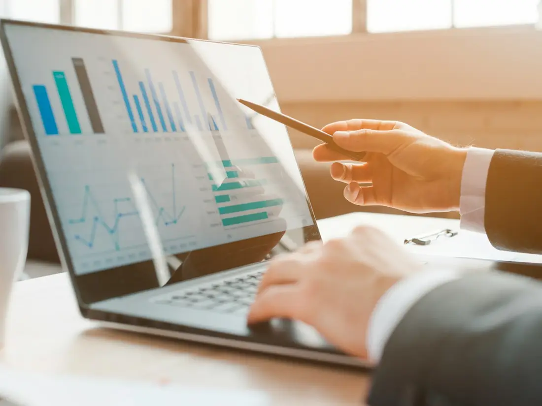 A hand pointing to charts on a laptop screen