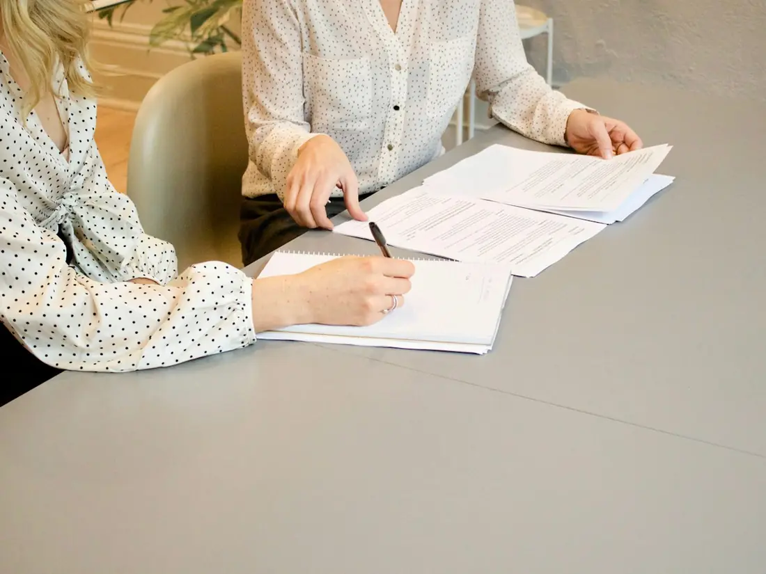 Two women signing paperwork together at a table