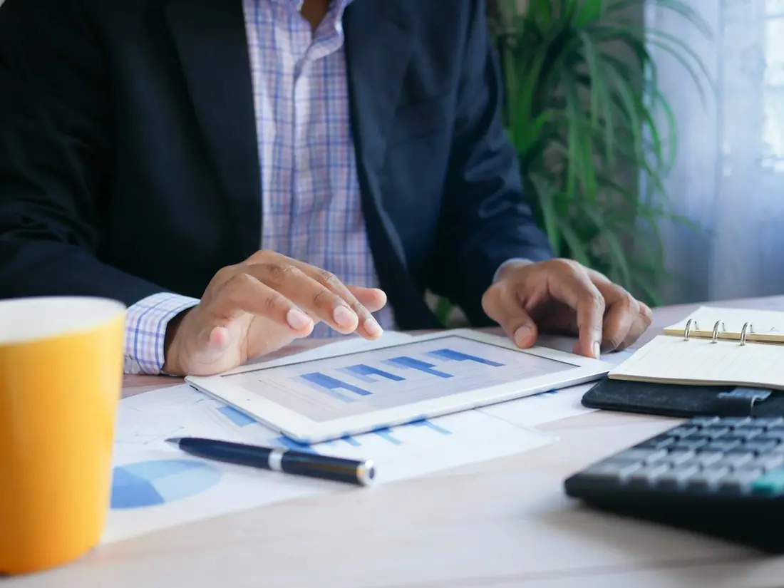 A person reviewing a printed chart with a tablet and a calculator on the desk